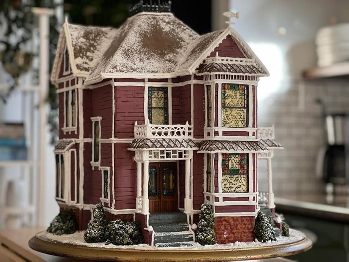 A meticulously crafted gingerbread house with a snowy roof, colorful stained-glass windows, and intricate icing details, displayed indoors.