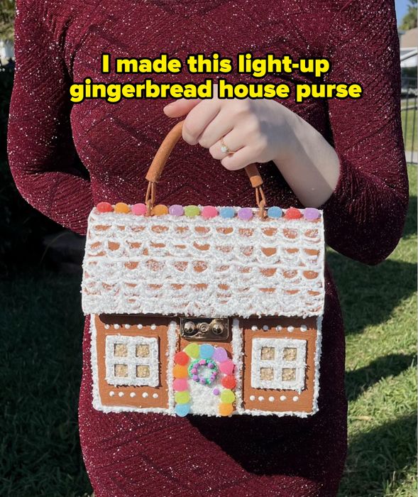 A person holding a handbag shaped like a gingerbread house, wearing an elegant textured dress