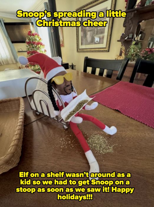 An Elf doll dressed in Christmas attire, sitting on a table, wearing sunglasses and holding a paper with herbs, beside a holiday decoration