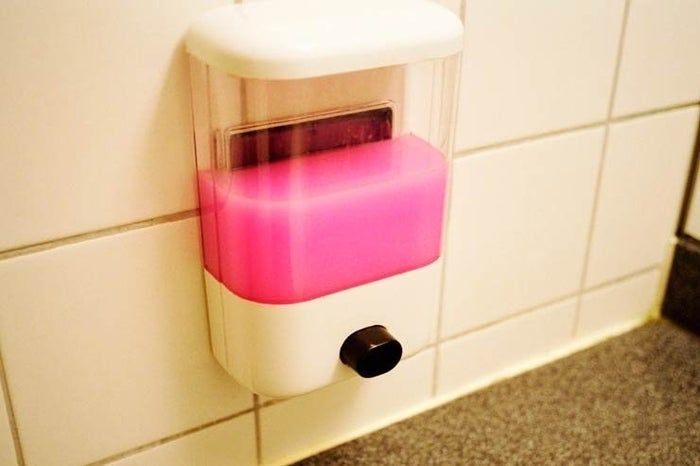 A soap dispenser mounted on a tiled surface, filled with pink liquid soap.