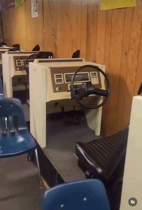 Vintage driver's education simulators featuring steering wheels and dashboard controls, often found in classroom environments.