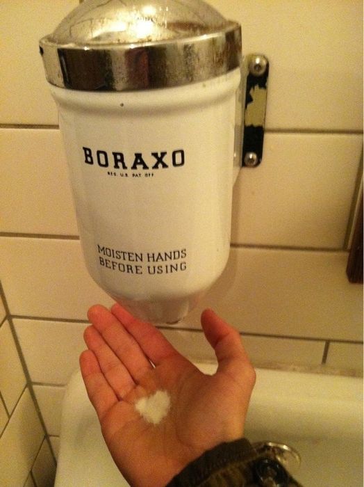 A hand reaching for Boraxo powdered soap from a dispenser, accompanied by a 