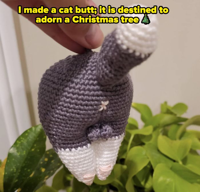 A crocheted cat's rear end being held above a plant, showcasing its tail and hind legs.