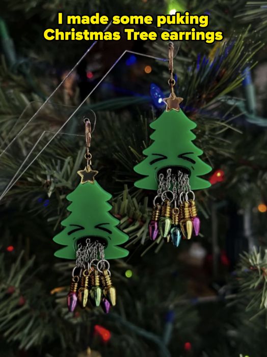 Earrings in the shape of festive trees, adorned with colorful bulb-like ornaments, hang from a Christmas tree branch