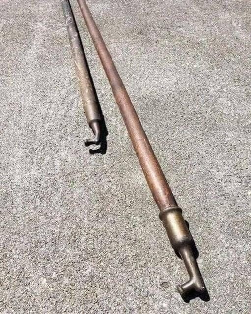 Two long, weathered metal pipes with hooked ends resting on a concrete surface.