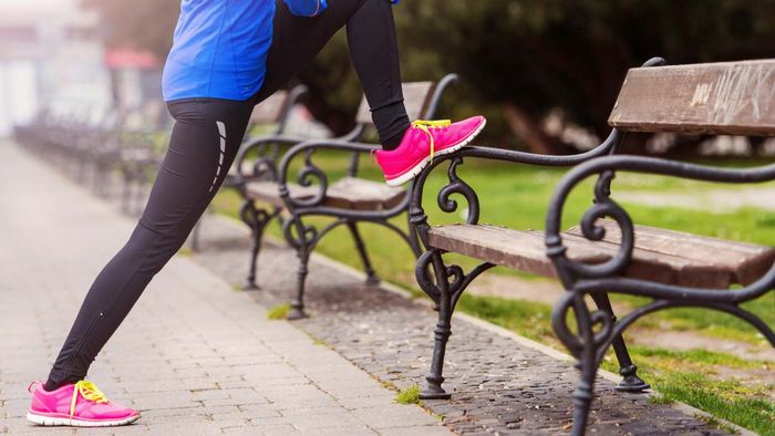 a runner performing stretches on a park bench