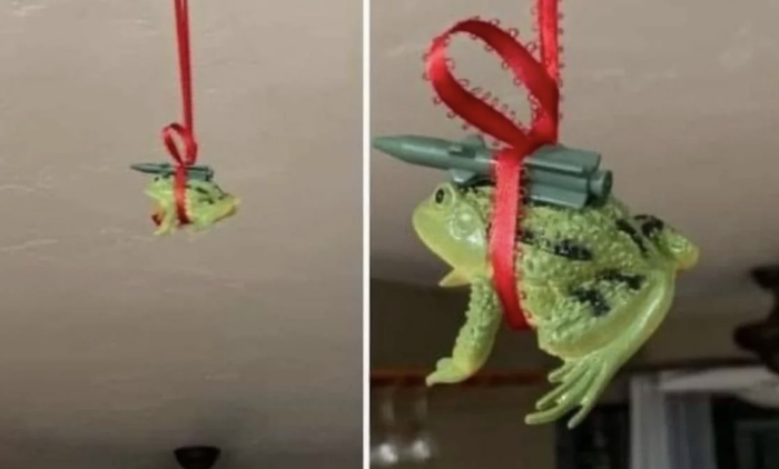 A frog ornament adorned with a red ribbon, carrying miniature toy missiles on its back, suspended from the ceiling.