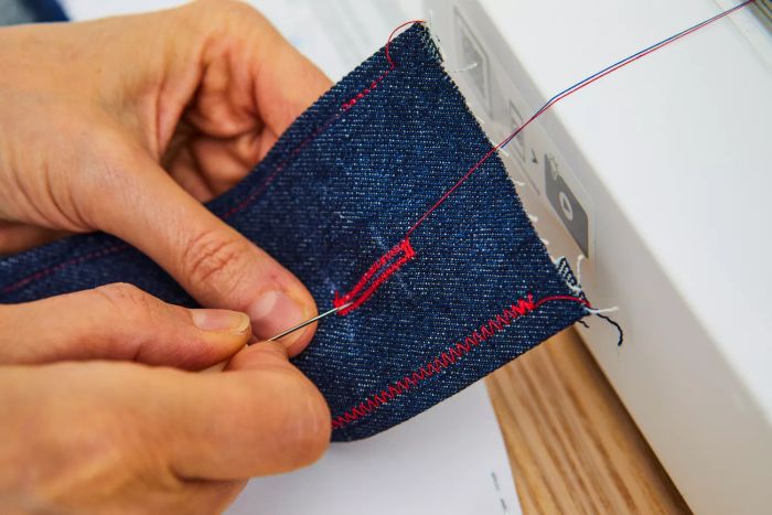 A pair of hands skillfully sewing a design into denim fabric.