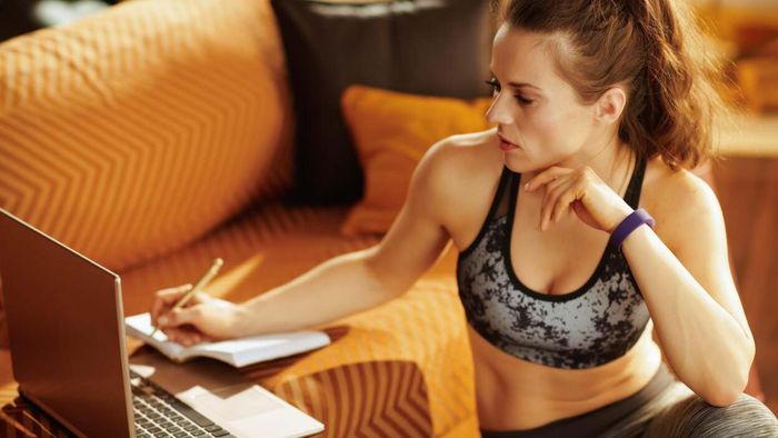 A woman in workout gear, jotting down notes in her training journal.