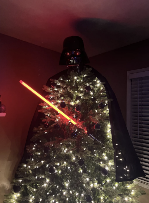 A Christmas tree adorned with a Darth Vader mask, cape, and a red lightsaber, capturing the essence of the Star Wars character.