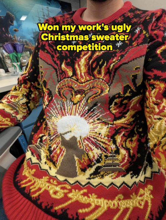 A person wearing a sweater with a bold, complex flame and sunburst pattern, sitting indoors.