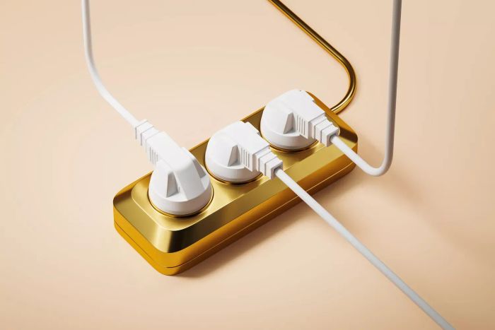 A golden electrical extension cord featuring three sockets and connected plugs, set against a beige backdrop. Symbolizes the increasing cost of electricity.