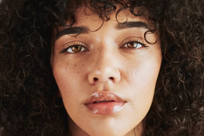 A studio portrait of a black woman showcasing the beauty and benefits of natural skincare or treatments. The image captures her gently touching her cheek after a skincare routine.