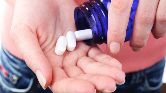 A woman takes three small white tablets from a blue glass bottle and holds them in her palm.