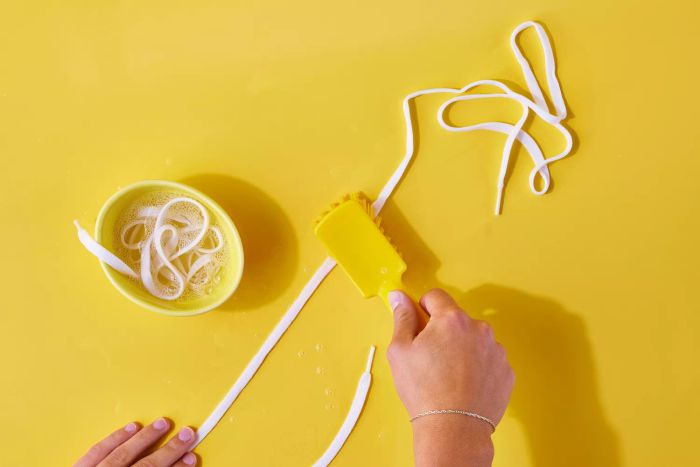 Shoelaces being scrubbed clean with a bristle brush
