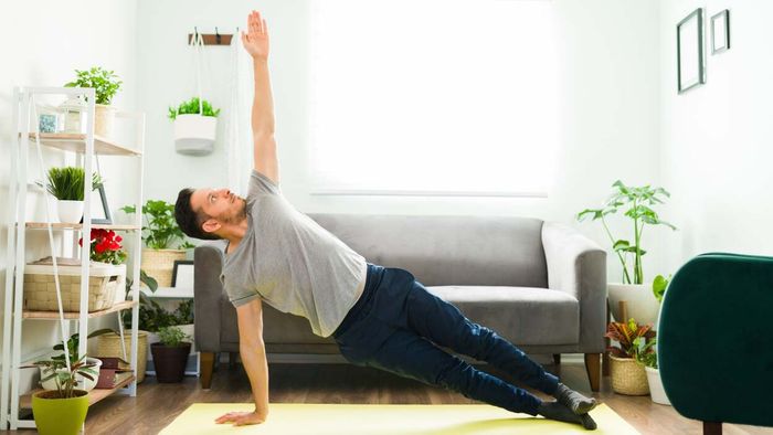 A man stretches sideways in his living room on a yoga mat