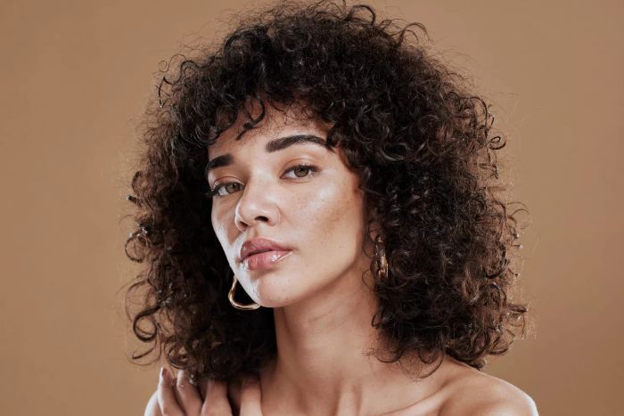 Natural hair, portrait of a Black woman in a studio setting promoting cosmetics, makeup, and beauty salon services. A close-up headshot of a young model with glowing skin, shiny hair, and healthy hair care.