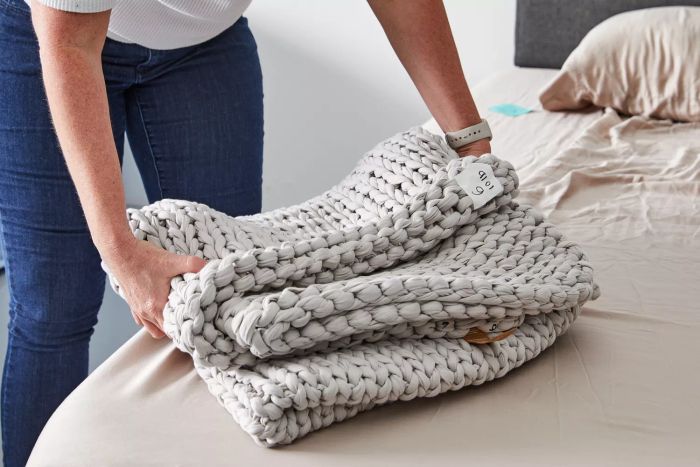 A person placing a neatly folded Bearaby Cotton Weighted Blanket on a bed