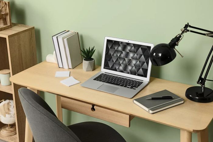 A contemporary laptop, books, lamp, and stationery arranged on a wooden desk beside a green wall