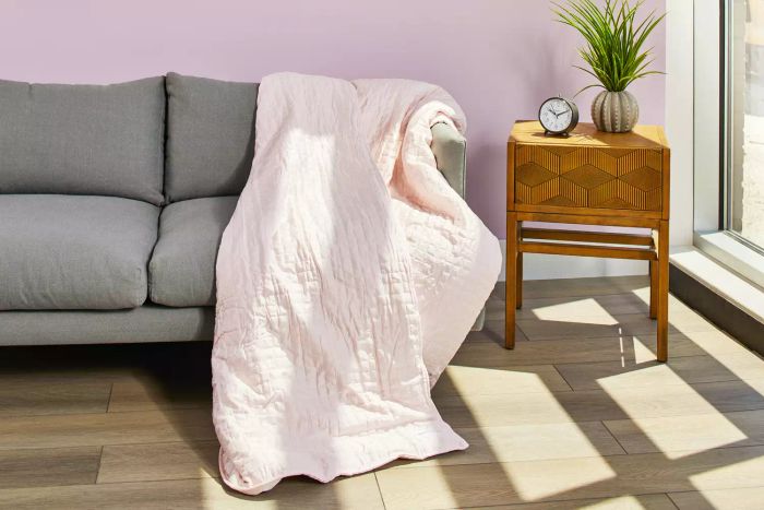 The Gravity Cooling Weighted Blanket neatly placed on a gray couch beside a side table