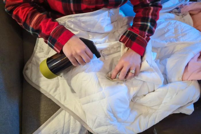 A person spot-cleaning the Aricove Cooling Weighted Blanket with a spray