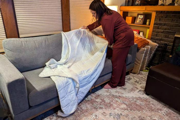 A person arranging the Aricove Cooling Weighted Blanket on a couch