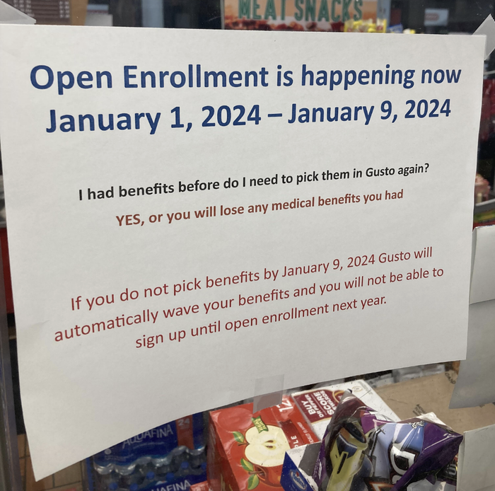 The sign says: 'Open Enrollment is now from January 1, 2024, to January 9, 2024; select your benefits by January 9, 2024, or forfeit your medical benefits. Failure to select will result in automatic loss.'