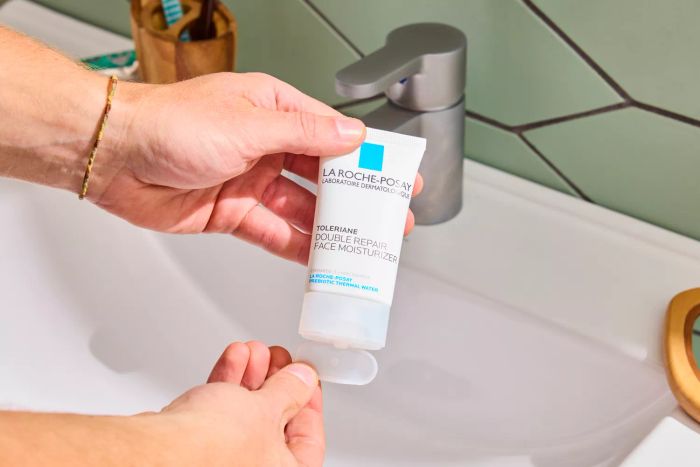A person holding the La Roche-Posay Toleriane Double Repair Face Moisturizer next to a sink