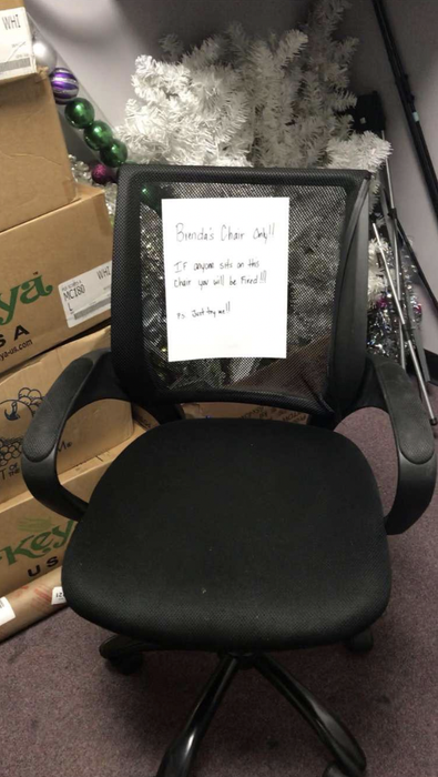 A photo of the chair in question, displaying a sign that reads 'Brenda's chair only. Anyone who sits here will be fired. P.S. Just try me.'