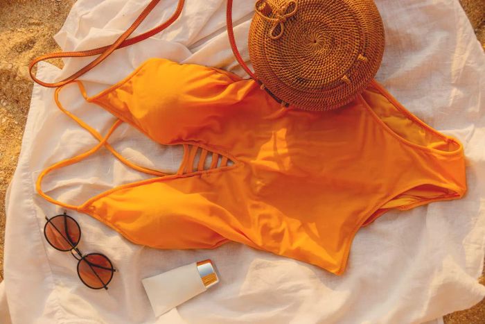 A stunning yellow swimsuit, paired with glasses and sunscreen on a sandy beach. Perfect for a summer vacation getaway.