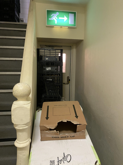 The fire escape is entirely blocked by a pile of boxes and crates