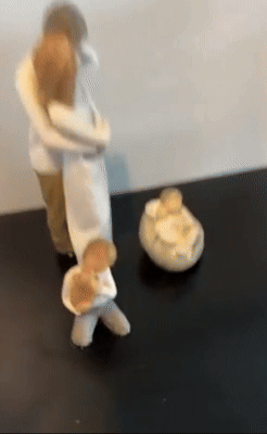 Wooden carvings depicting a family: two adults hugging, a child walking, and a baby resting in a basket