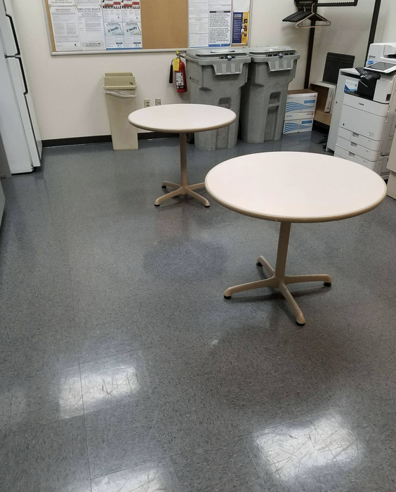 A break room featuring two round tables, recycling bins, a fire extinguisher, a bulletin board, a copier, and assorted office supplies.