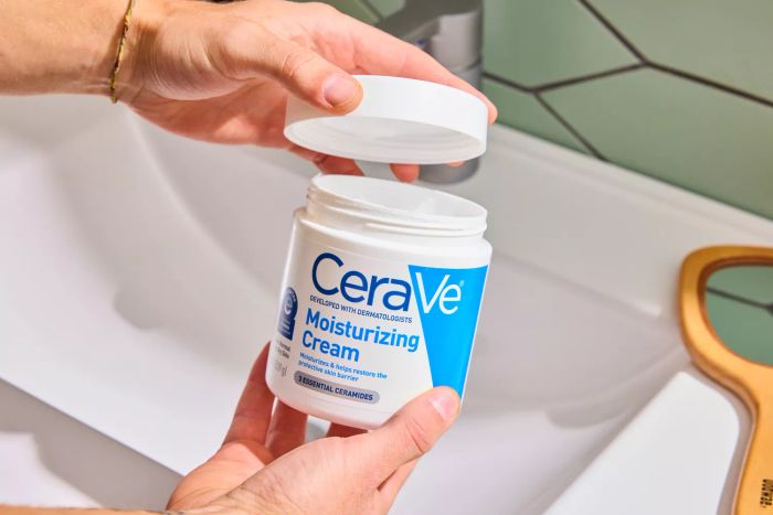 A person holding the lid and container of the CeraVe Moisturizing Cream