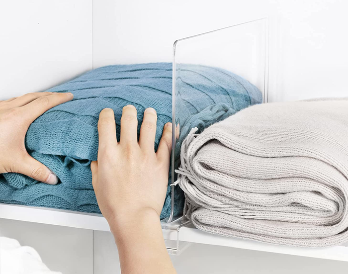 A model organizing towels on a shelf with the clear dividers in place