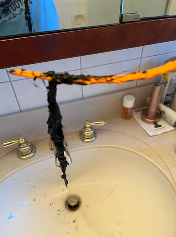 A clogged bathroom sink drain with a tool removing hair and debris