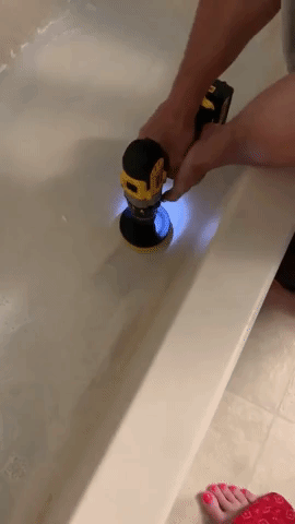 A reviewer using the brush to clean stubborn grime from a bathtub