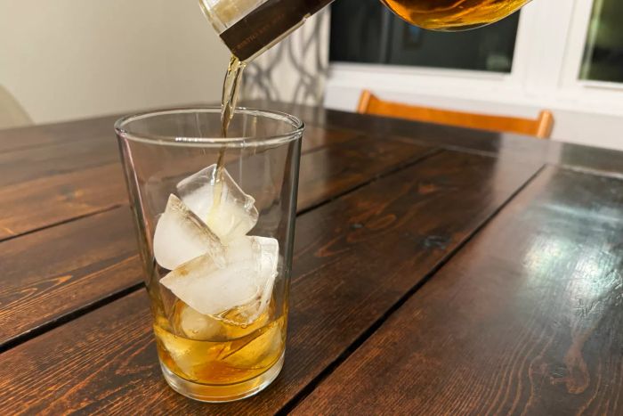 A person pouring liquid into a Duralex Unie Glass Tumbler filled with ice cubes