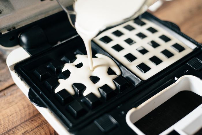 A person pouring batter into a waffle iron.