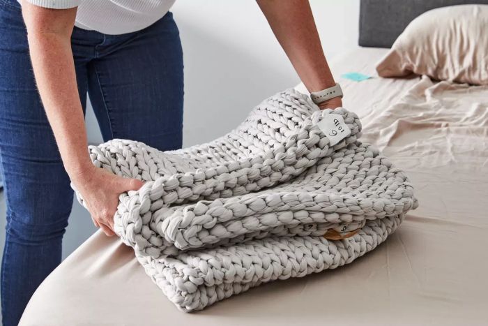 A person placing a neatly folded Bearaby Cotton Weighted Blanket on a bed