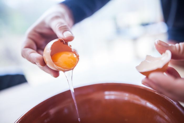 A person cracking an egg into a mixing bowl.