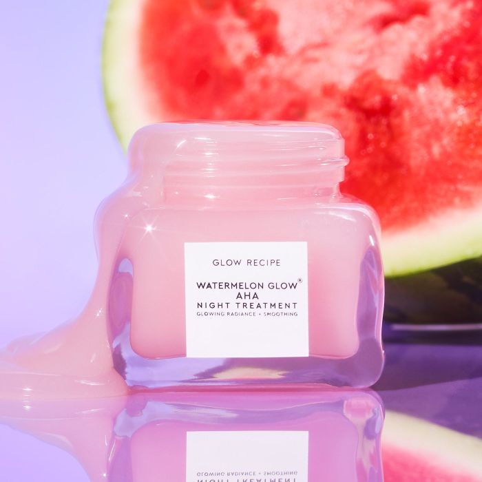 A jar of Glow Recipe Watermelon Glow AHA Night Treatment with a scoop of pink gel spilled around it, accompanied by a watermelon slice in the background