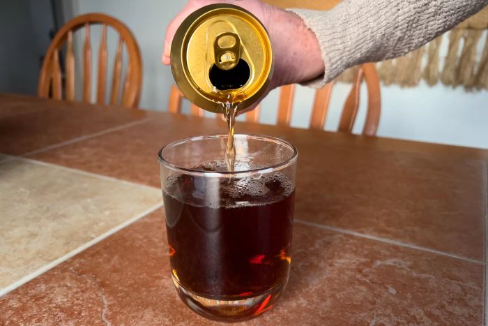 A person pouring soda into a Libbey Polaris 16-Piece Tumbler and Rocks Glass Set glass