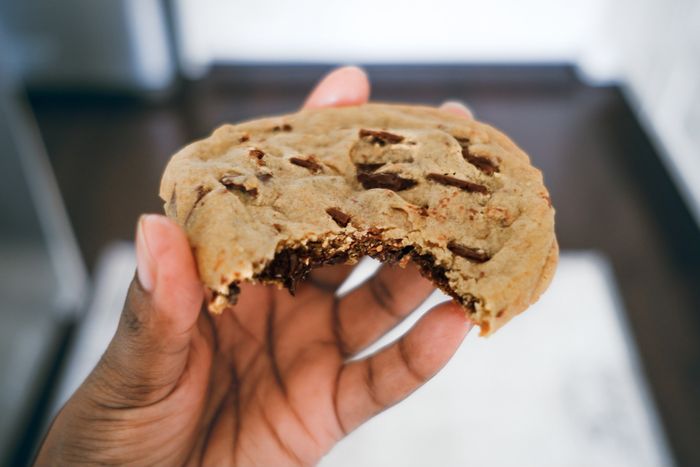 A woman holding a half-eaten chocolate chip cookie.