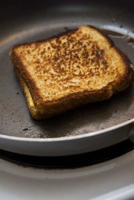 A golden-brown grilled cheese sandwich sizzling in a frying pan on the stove.