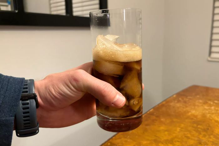 A person holding a glass from the Luigi Bormioli Set of 4 Classico Tall Beverage Set, filled with soda and ice