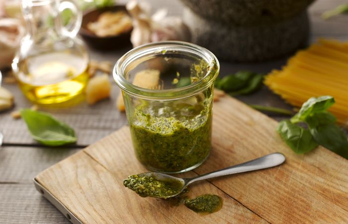 A jar of pesto and a spoon placed on a wooden cutting board.