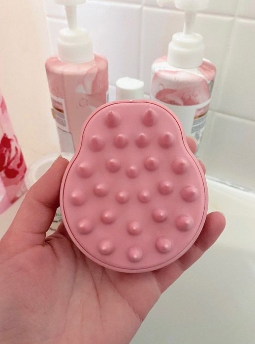 A Mytour editor holding a pink scalp massager featuring soft silicone bristles