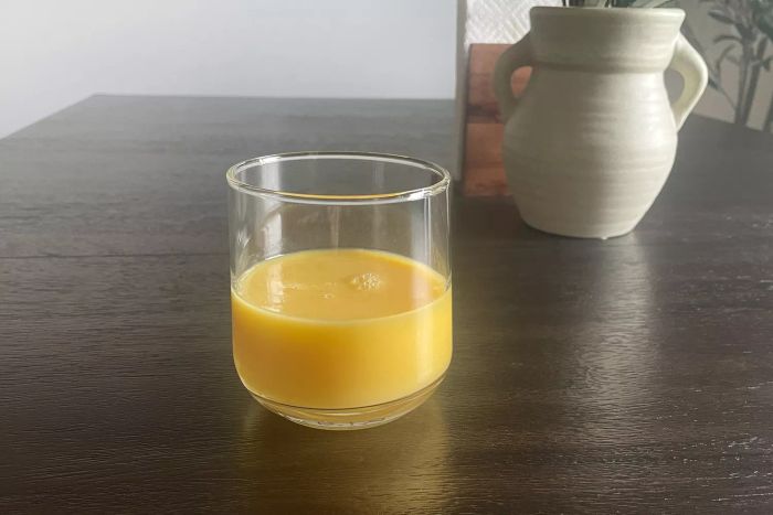 A Libbey Ascent 16-Piece Assorted Glassware Set glass half-filled with orange juice, placed on a wooden table
