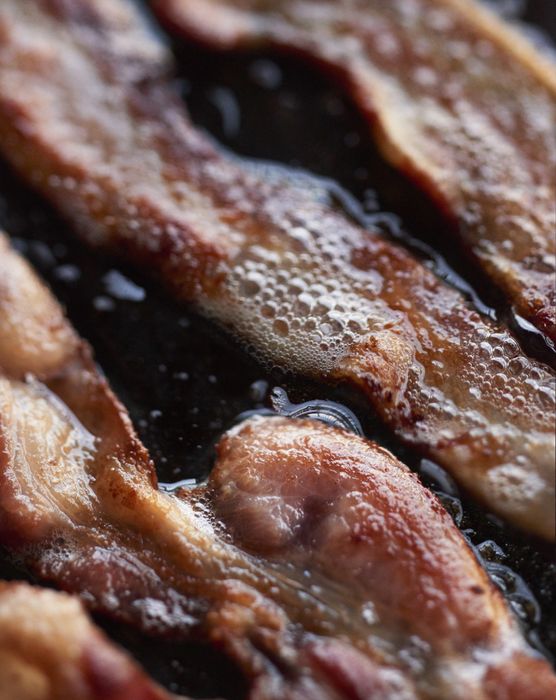 Bacon strips sizzling in a skillet.